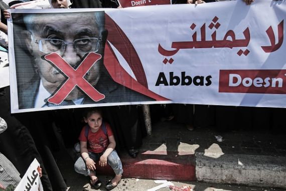 فتاة تجلس تحت لافتة تحمل صورة مقاطعة للرئيس الفلسطيني أثناء مظاهرة نظمها أنصار حماس ضد عباس في غزة