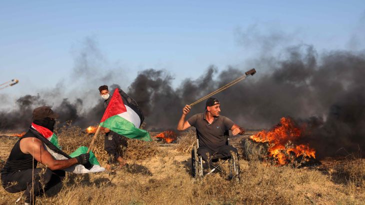 متظاهر فلسطيني يستخدم مقلاعًا لإلقاء الحجارة على الجنود الإسرائيليين خلال مسيرة بالقرب من السياج الحدودي