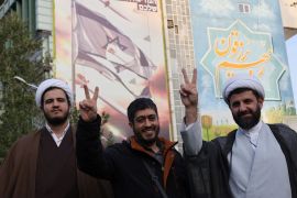 رجل دين إيراني يظهر علامة النصر أمام لوحة إعلانية مناهضة لإسرائيل خلال احتفال عقب الهجوم الإيراني على إسرائيل (رويترز)
